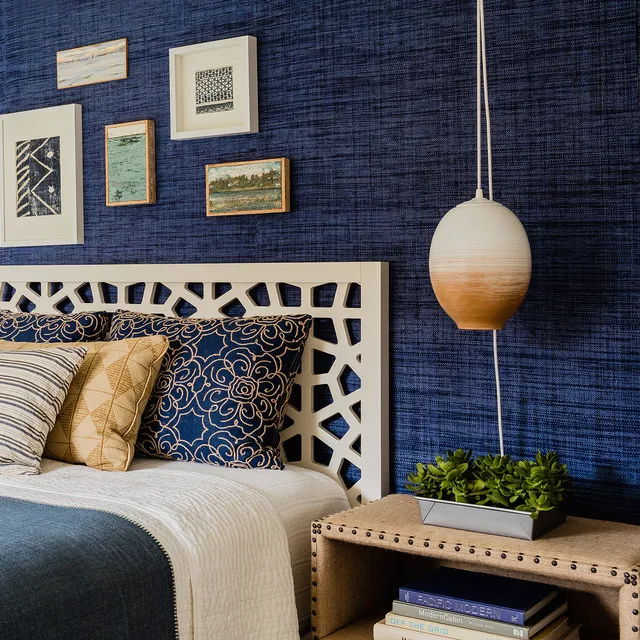 A dark blue textured wall sits behind a pale decorative headboard beside a rounded pendant.