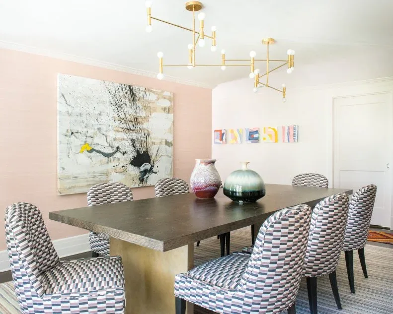 Two rounded decorative vases on a dark rectangular table with patterned chairs in a pink dining room