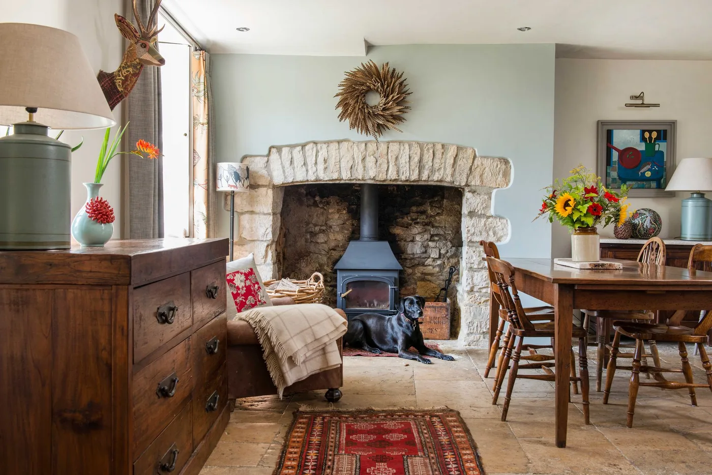 Dark stove inside pale stone opening in gray-green dining room with wooden dresser and dining furniture.