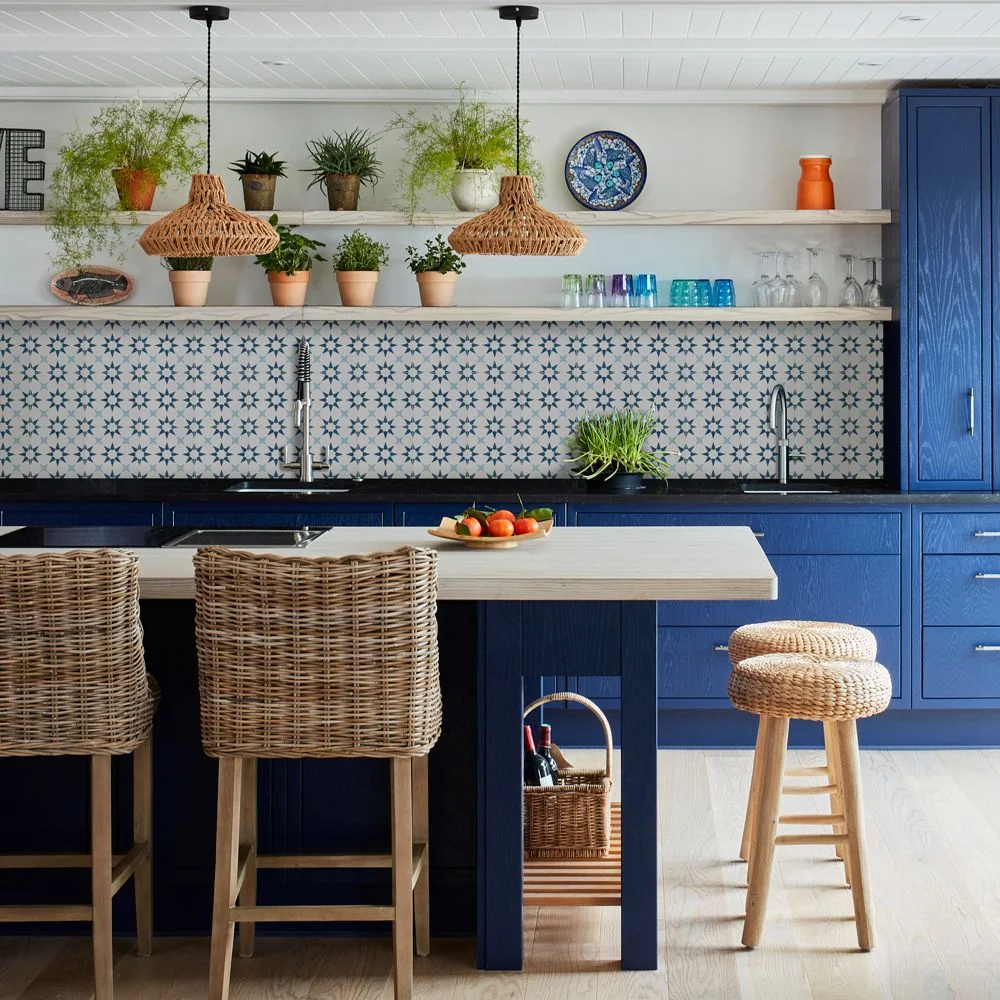 Blue-and-white patterned tiles run beneath shelves and plants beside blue kitchen cabinets and woven seating