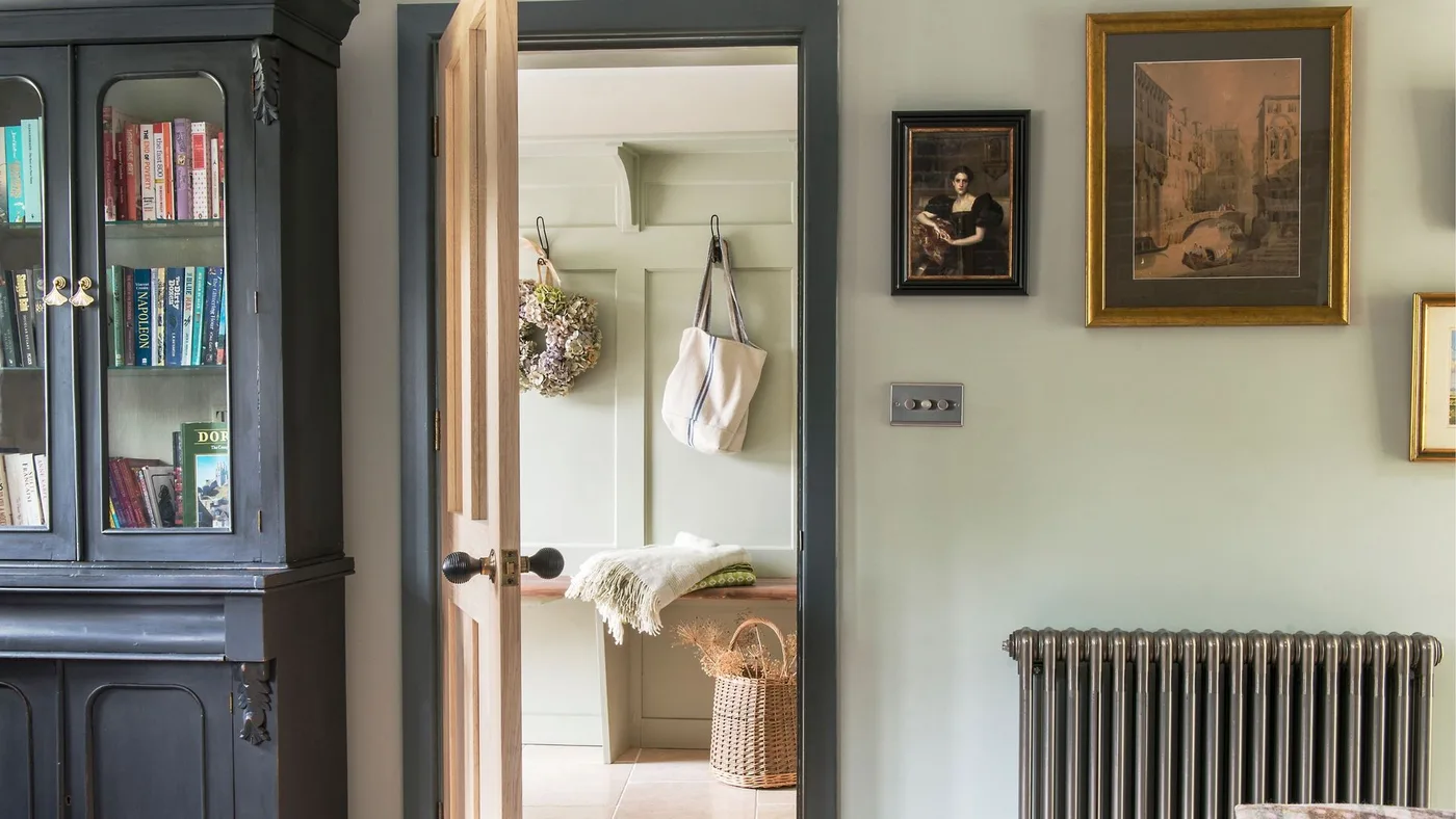 Green country hallway opening onto small paneled entry alcove with hooks, wood bench and woven basket
