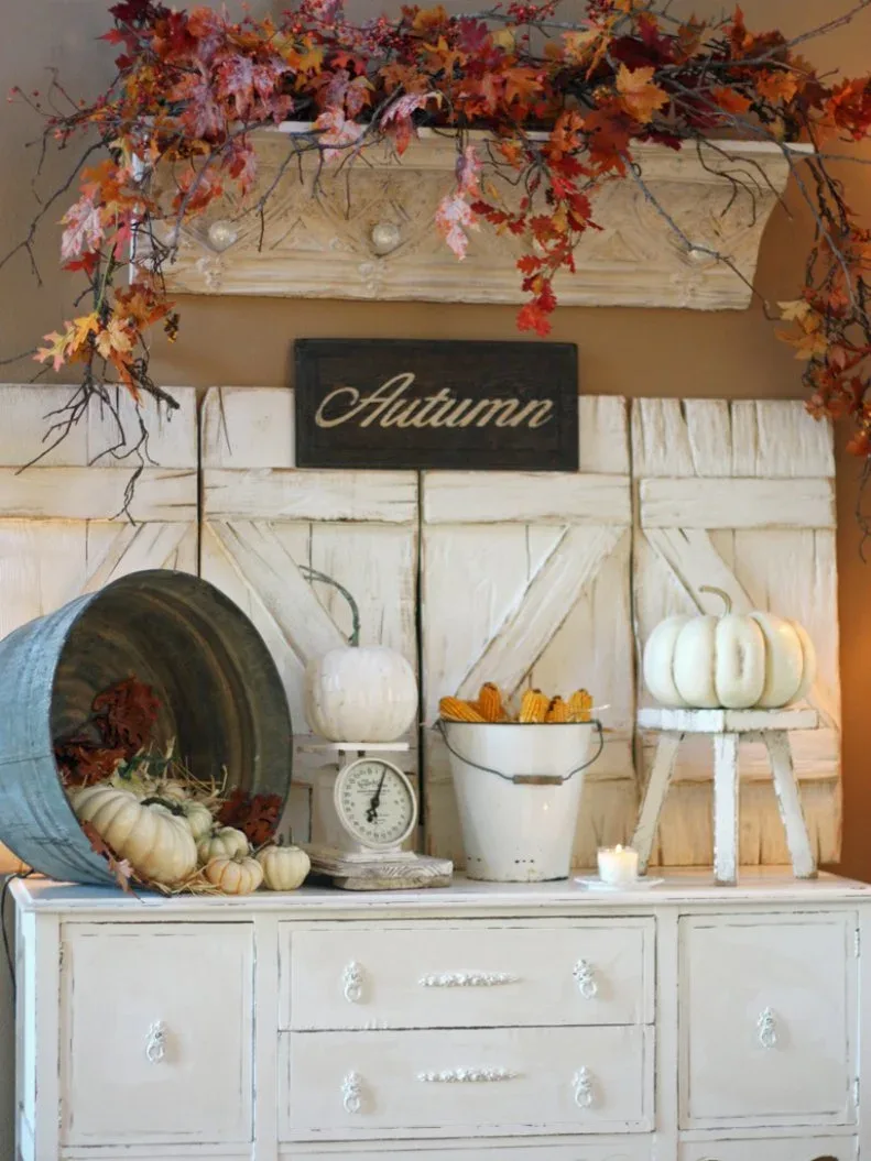 Painted entry chest with pumpkins, kitchen scale, foliage, autumn sign and pale bucket against white paneled backdrop