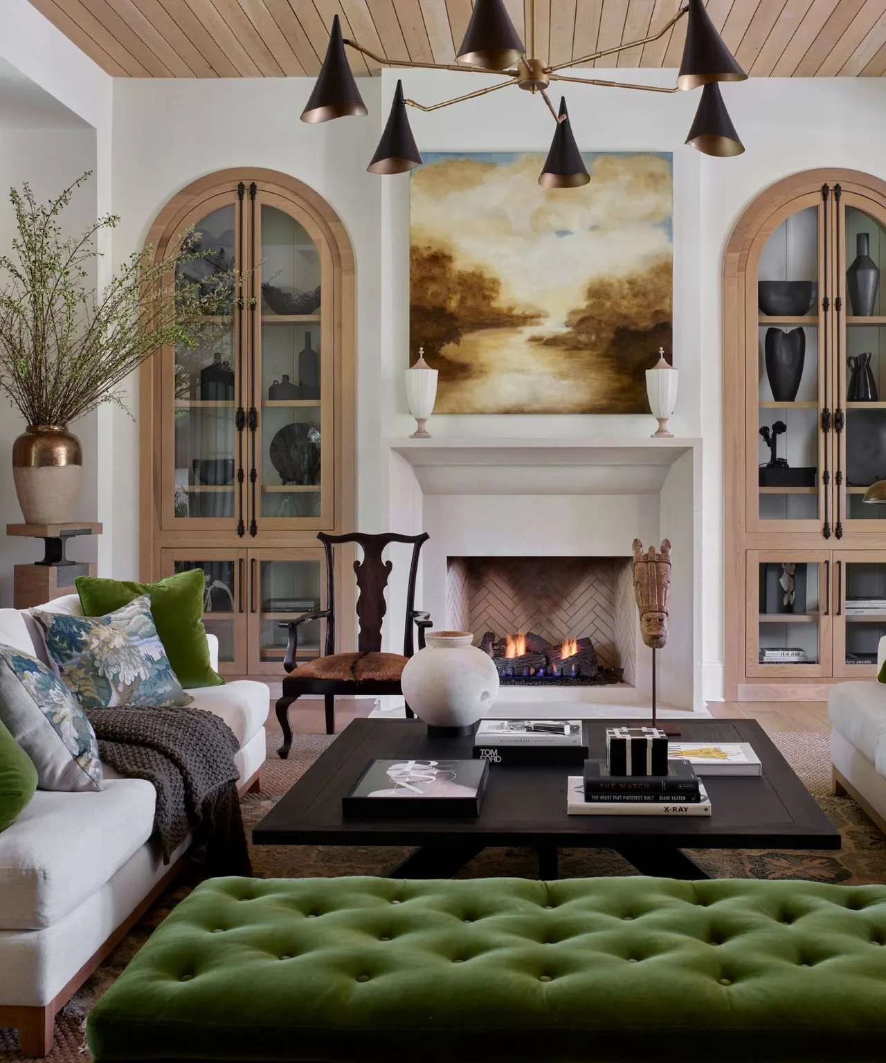 A green tufted ottoman sits among pale sofas and tall glazed cabinets.