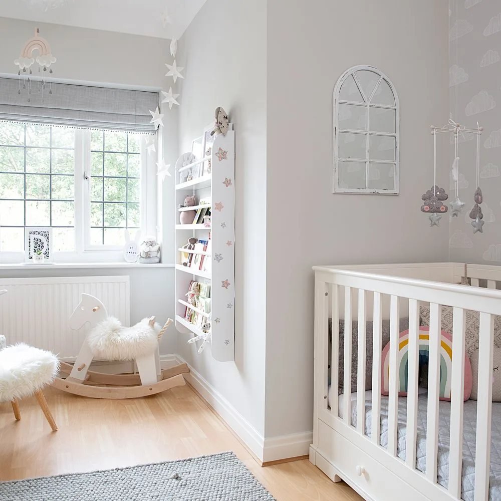 Pale crib and open bookcase in gray-and-white nursery with arched wall piece, rocking horse and wooden floor.