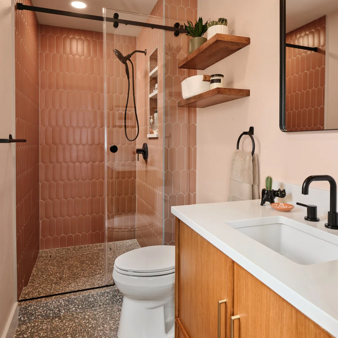 Peach-pink tiles with rounded ends line a shower beside black fittings, wooden shelves and a white sink