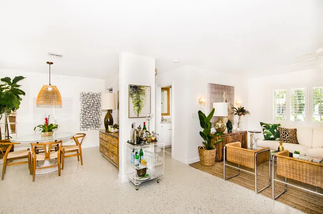 Woven seating and timber pieces sit within a pale open room beside plants.