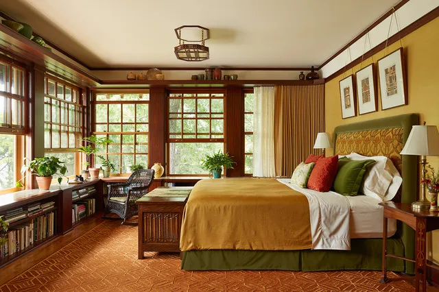 A gold coverlet brightens a timber-trimmed bedroom with large windows and a bedside lamp.