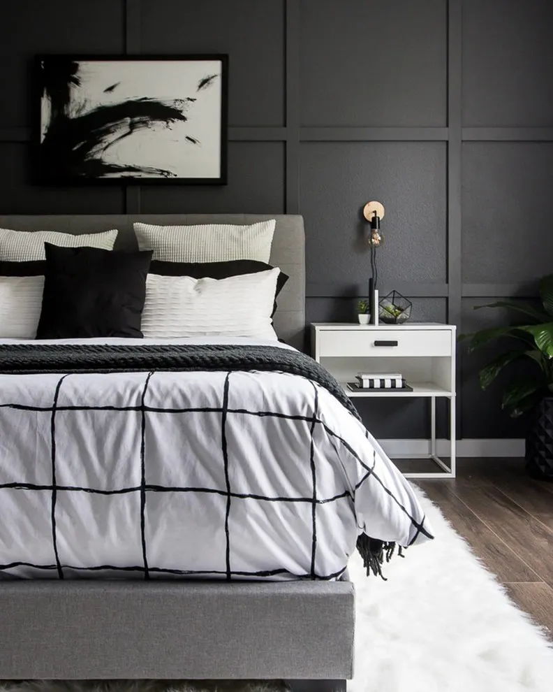 A black paneled wall sits behind a white bedcover with fine dark lines