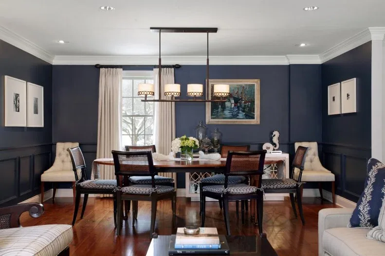 Navy dining room with dark chairs, pale curtains, white ceiling trim and a rectangular framed light.