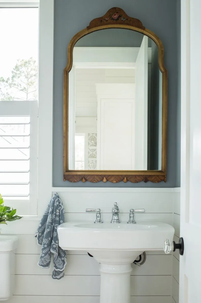 White paneled powder room with pedestal basin, pale blue wall and shaped wood mirror