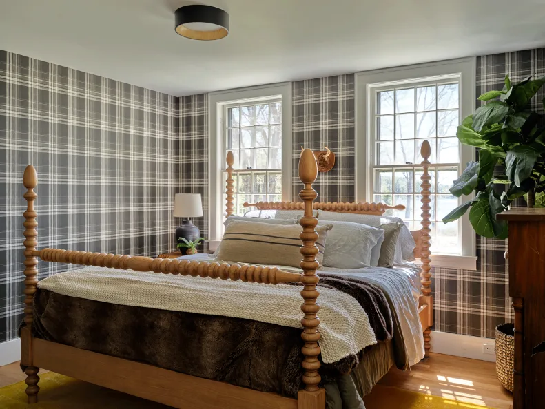 Bedroom with dark plaid wallpaper, turned wood bed, pale bedding and two windows