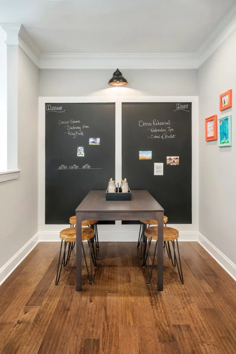 Small rectangular dining table and stools beneath a large double chalkboard and a wall light