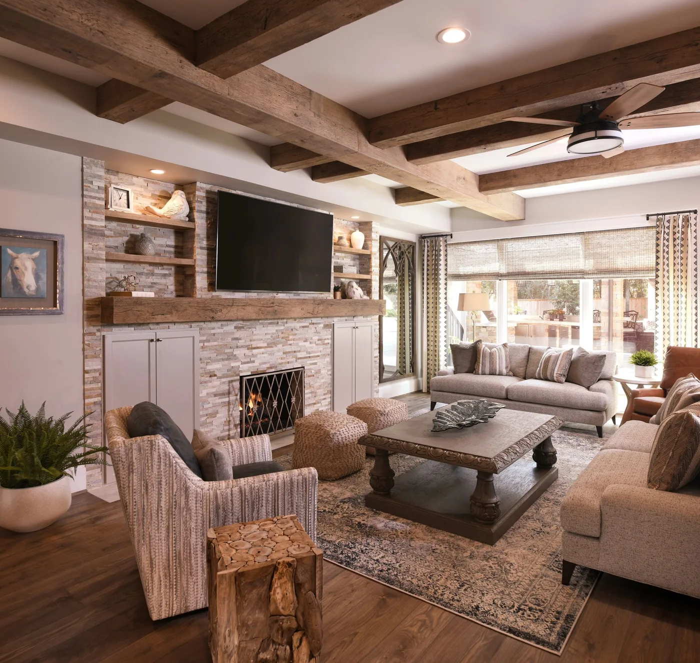 Textured pale fireplace wall with broad wood mantel, television, open shelves and lower cabinets beneath exposed beams