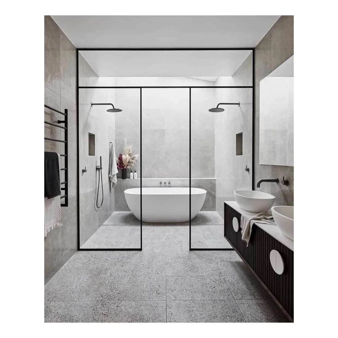 A black-framed glass enclosure surrounds a white tub and pale large-format walls above a speckled gray floor