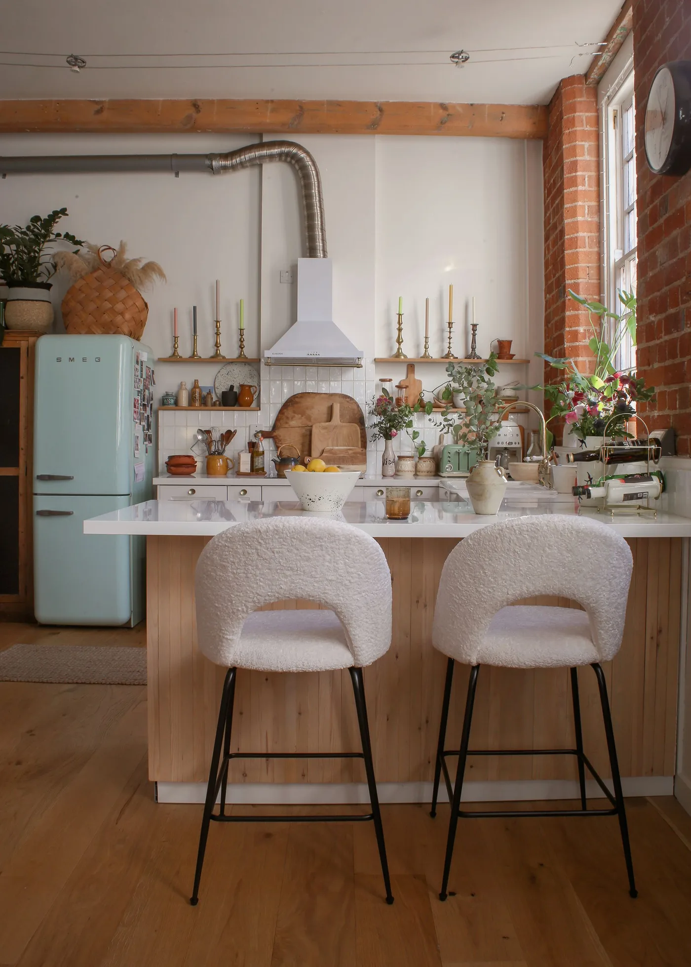 Kitchen with a pale green refrigerator, two pale rounded stools, a wood-fronted island and exposed brick.