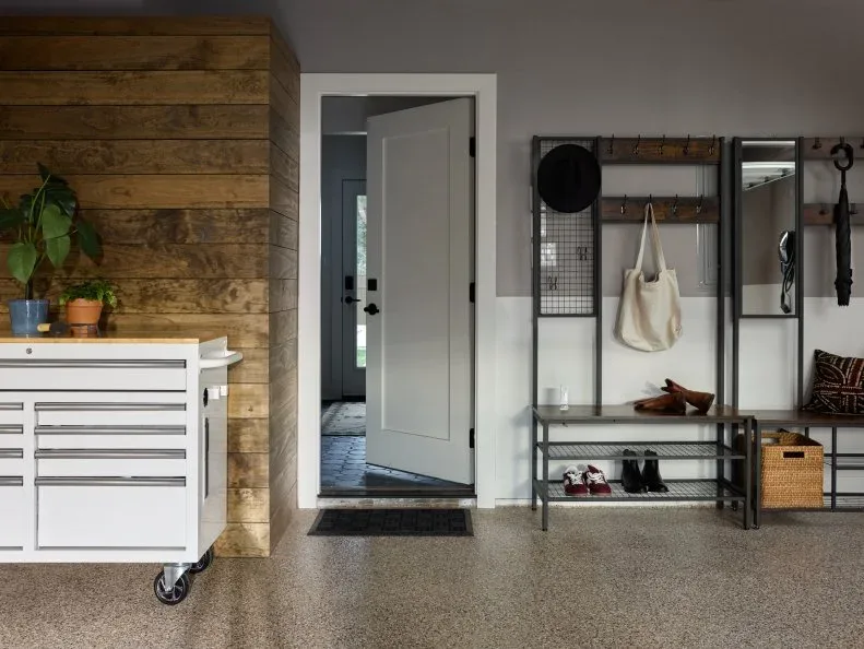 Freestanding dark hall stand with a bench, shoe shelf, coat hooks and mirror beside a garage-to-house door.