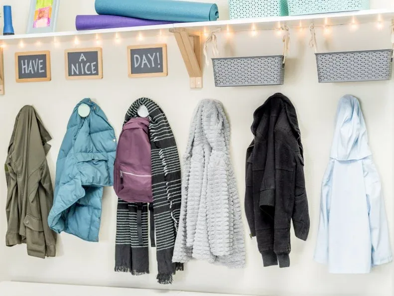 Row of coats and a backpack hanging beneath a white shelf with small baskets and colorful storage.