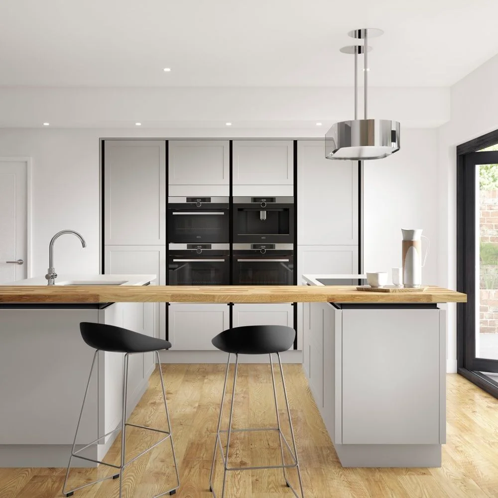 Two black kitchen stools sit at a straight wood breakfast ledge beside pale cupboard fronts, stacked appliances and a suspended metallic hood