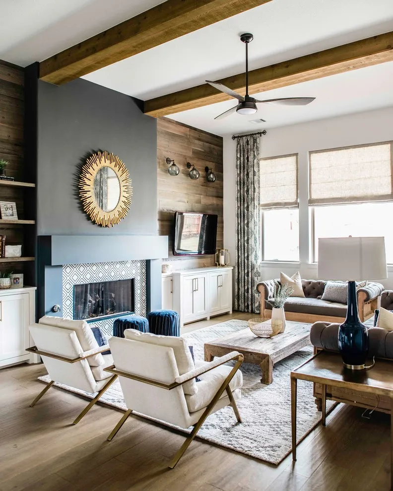 A gray-blue fireplace wall sits beneath timber beams beside pale chairs