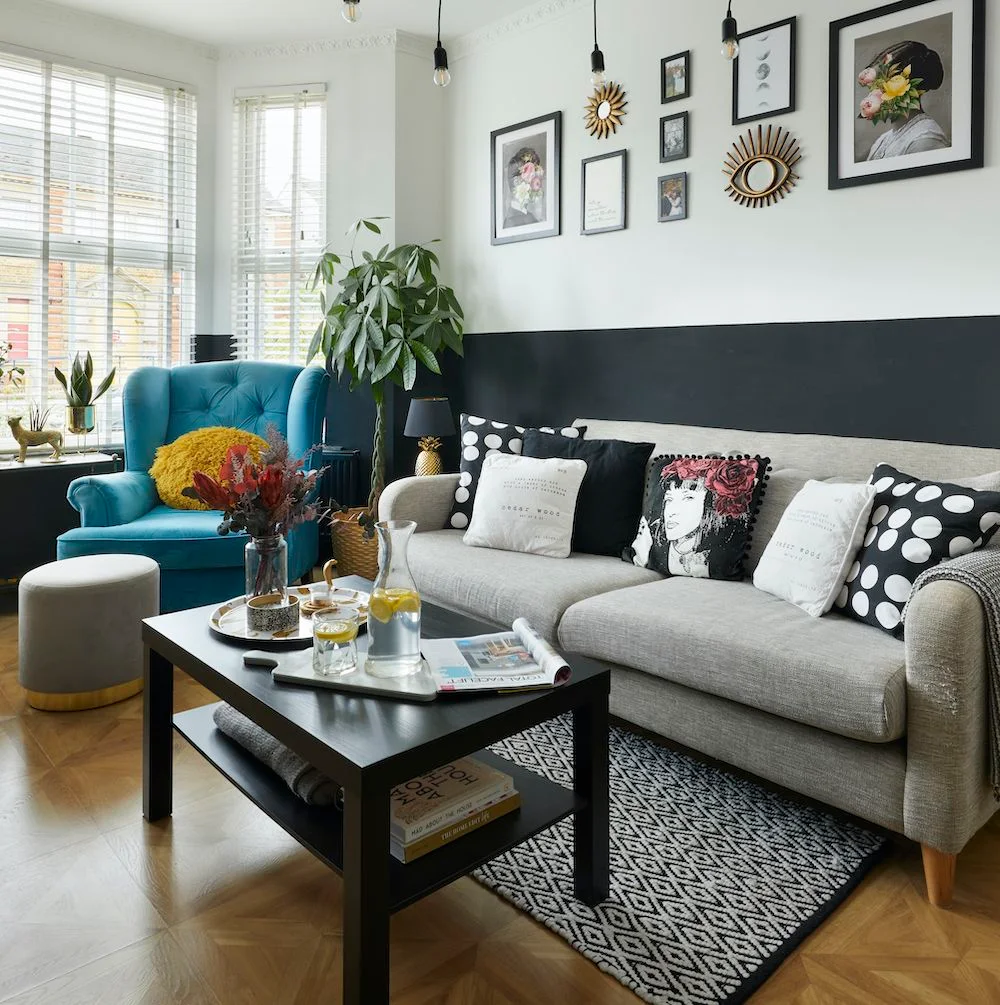 A light gray sofa with graphic cushions sits beneath black-framed artwork beside a turquoise chair and a black coffee table