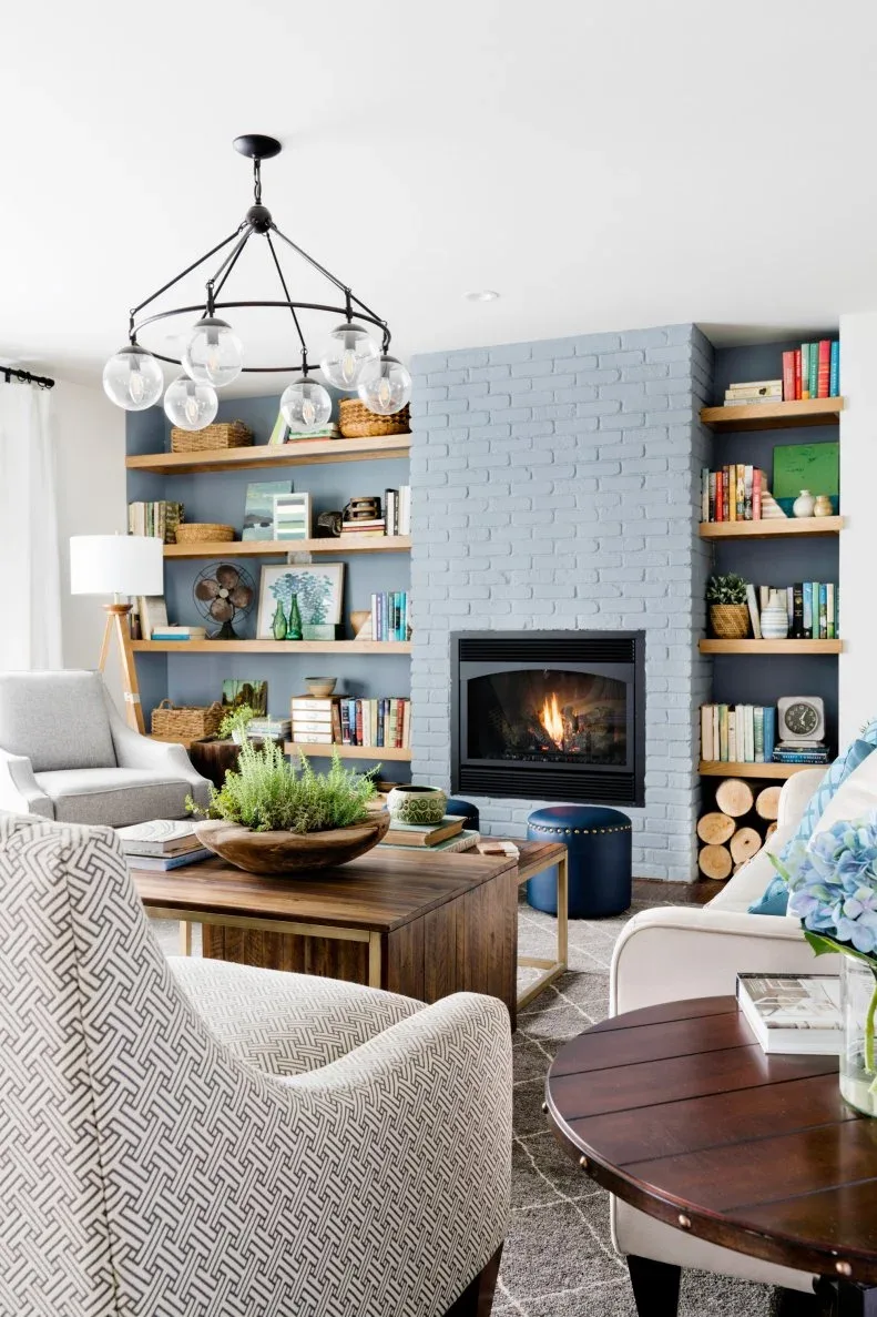 Pale blue-gray brick fireplace between wooden shelves filled with books, baskets and decorative pieces.