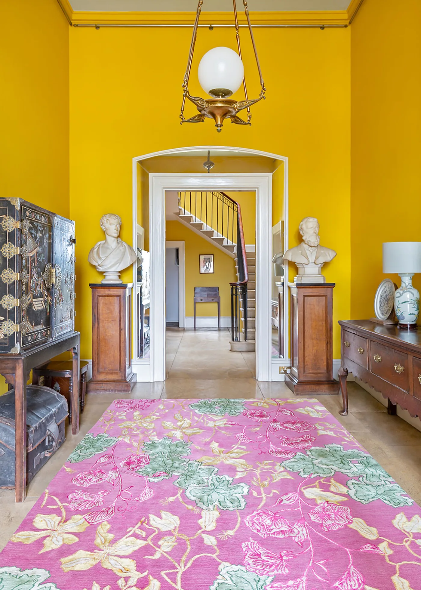 Pink floral rug beneath yellow walls, wood cabinets, white busts on pedestals and a traditional hanging lantern