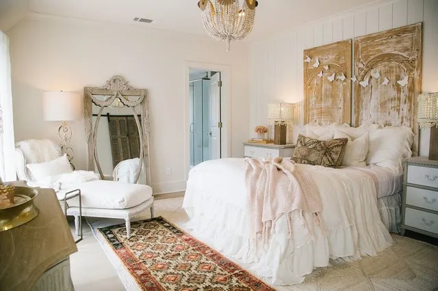A tall decorative headboard stands behind pale bedding beside a patterned rug.