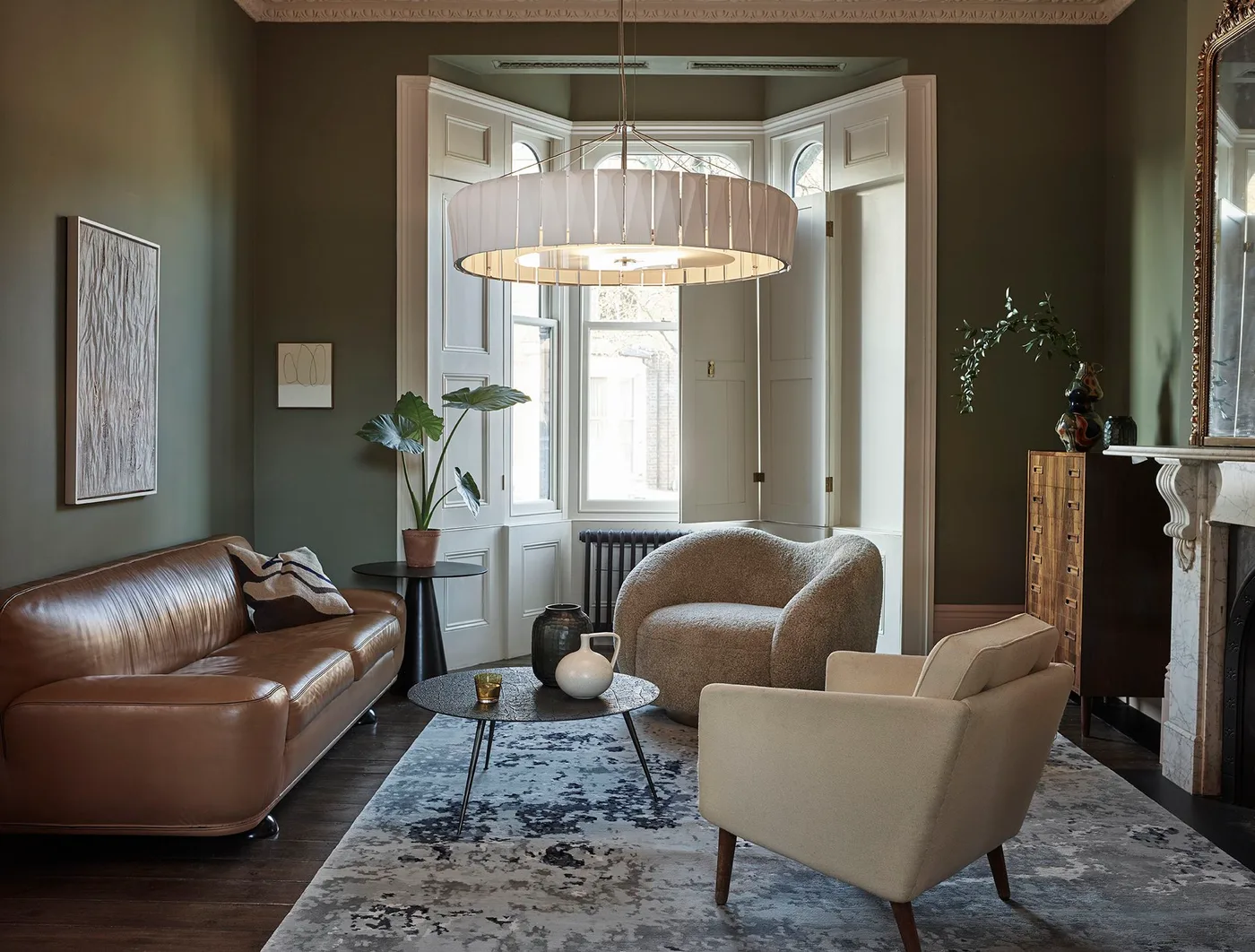 Moss green living room walls around a brown sofa, pale armchairs and a broad pendant near a bay window