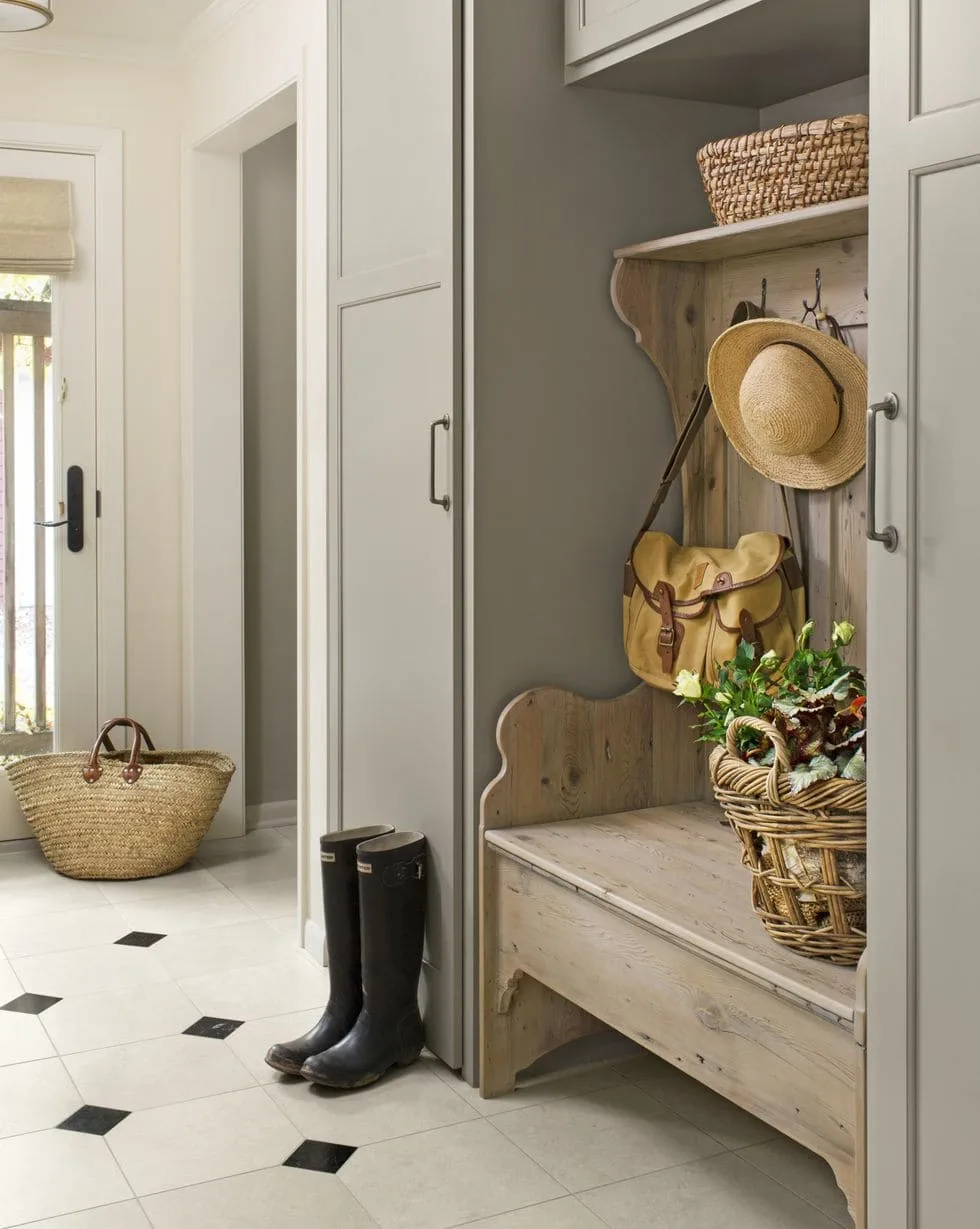 Rustic pale wooden bench with hooks and baskets between taupe cupboards in a mudroom.