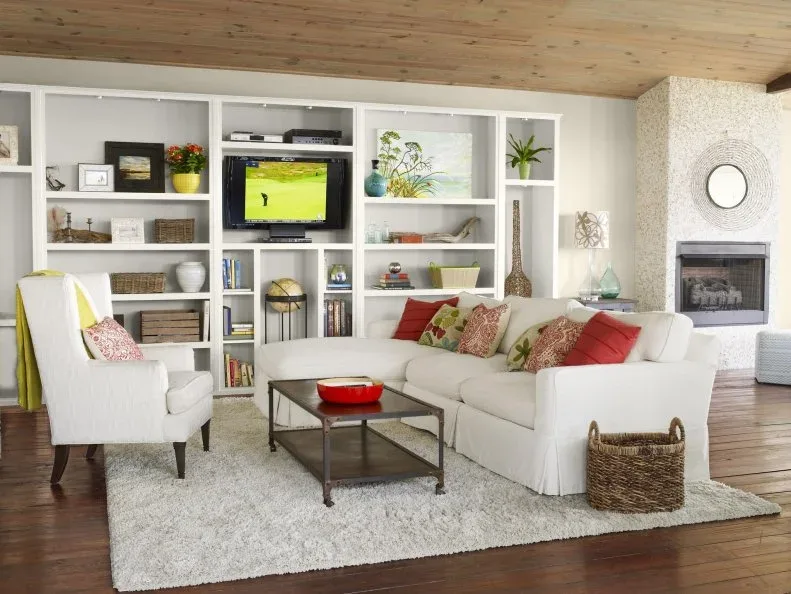White sofa and armchair in front of open shelves with red cushions, baskets and a warm wooden ceiling.
