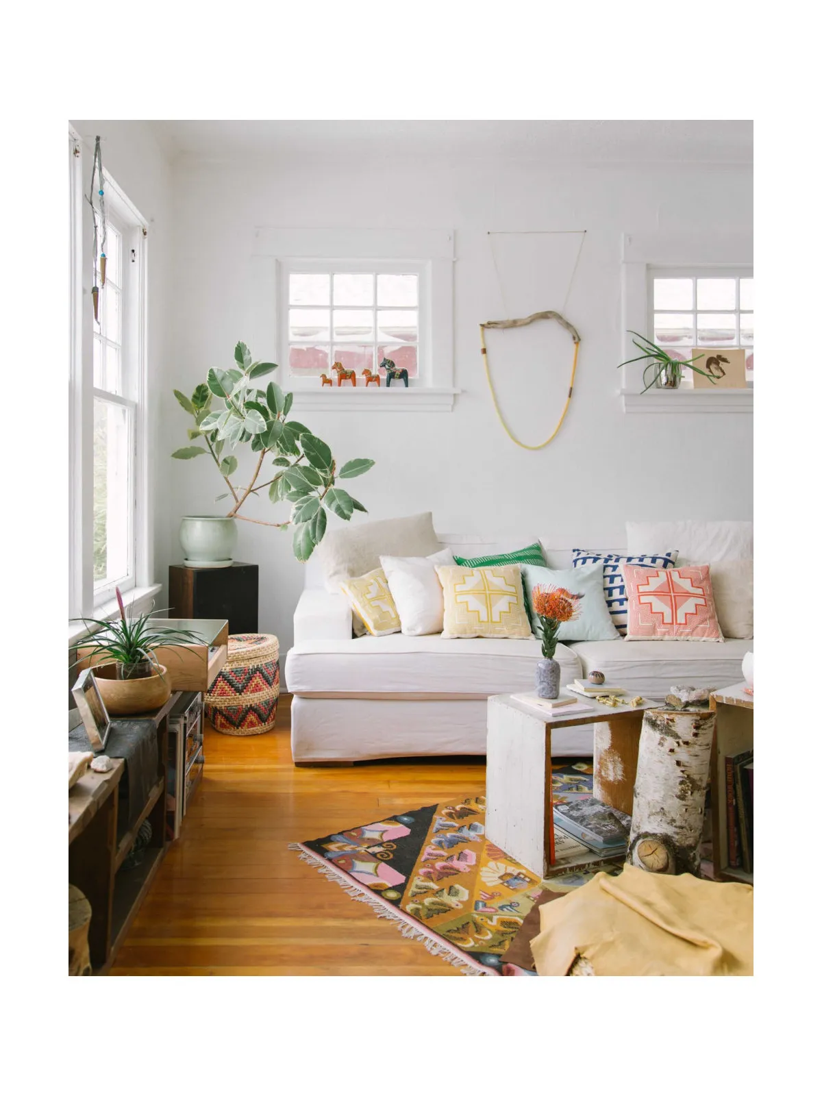 A pale sofa sits among plants, patterned cushions and varied smaller tables.