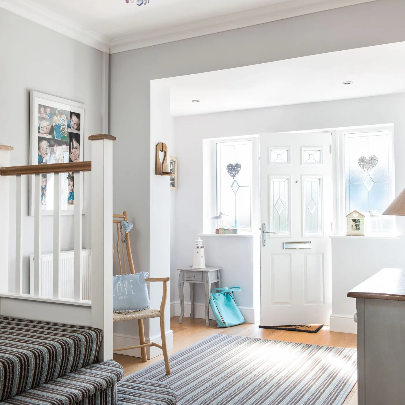 Large pale striped rug beside a wood chair, low side table and bright front door with glazed side panels