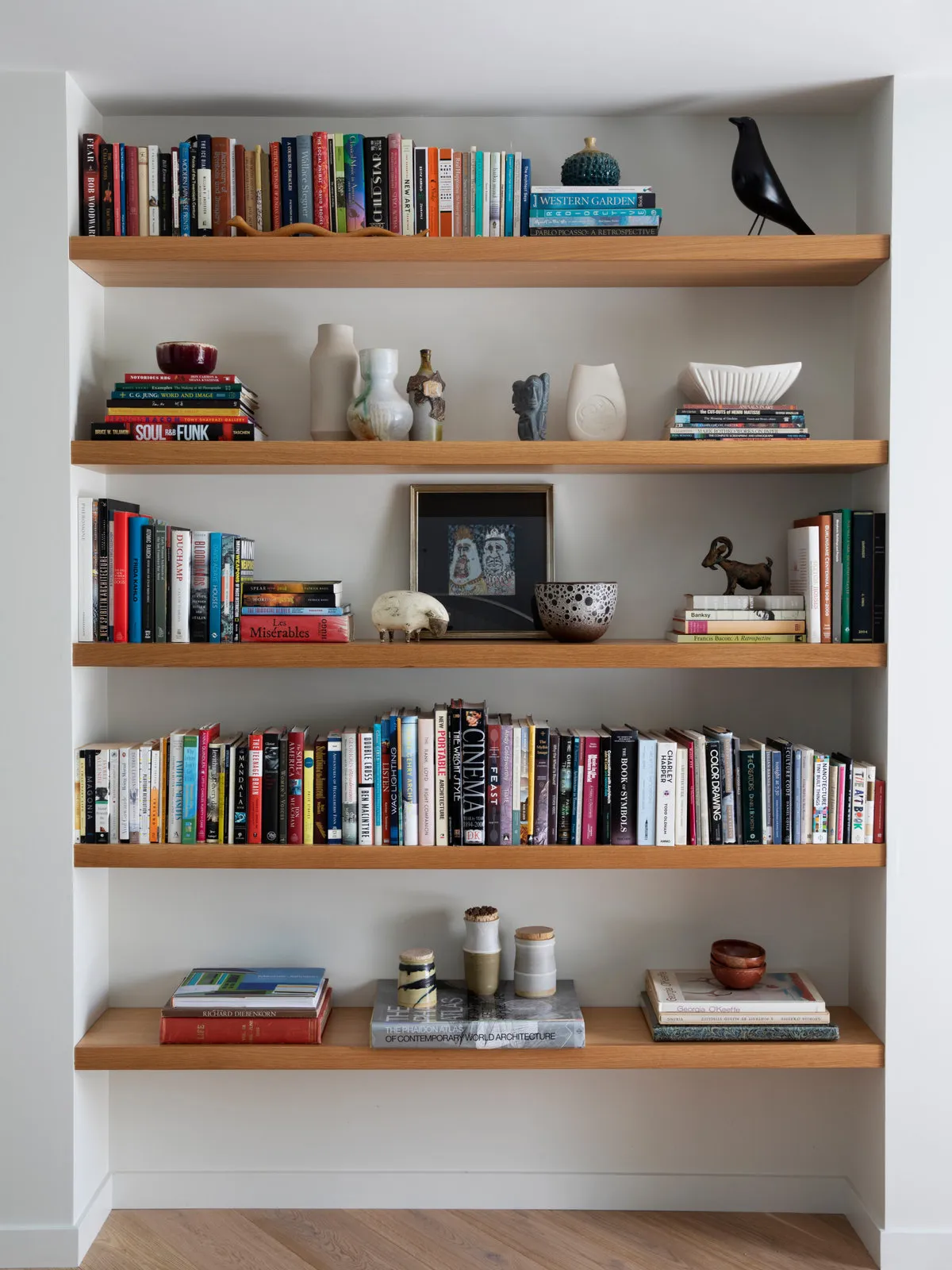 Simple timber shelves hold books and a few objects against a pale wall.