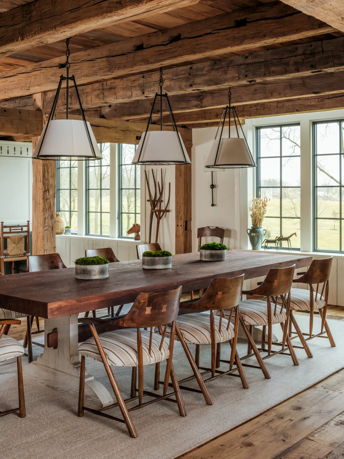 A long timber dining table stands beneath exposed beams and modest pendants.