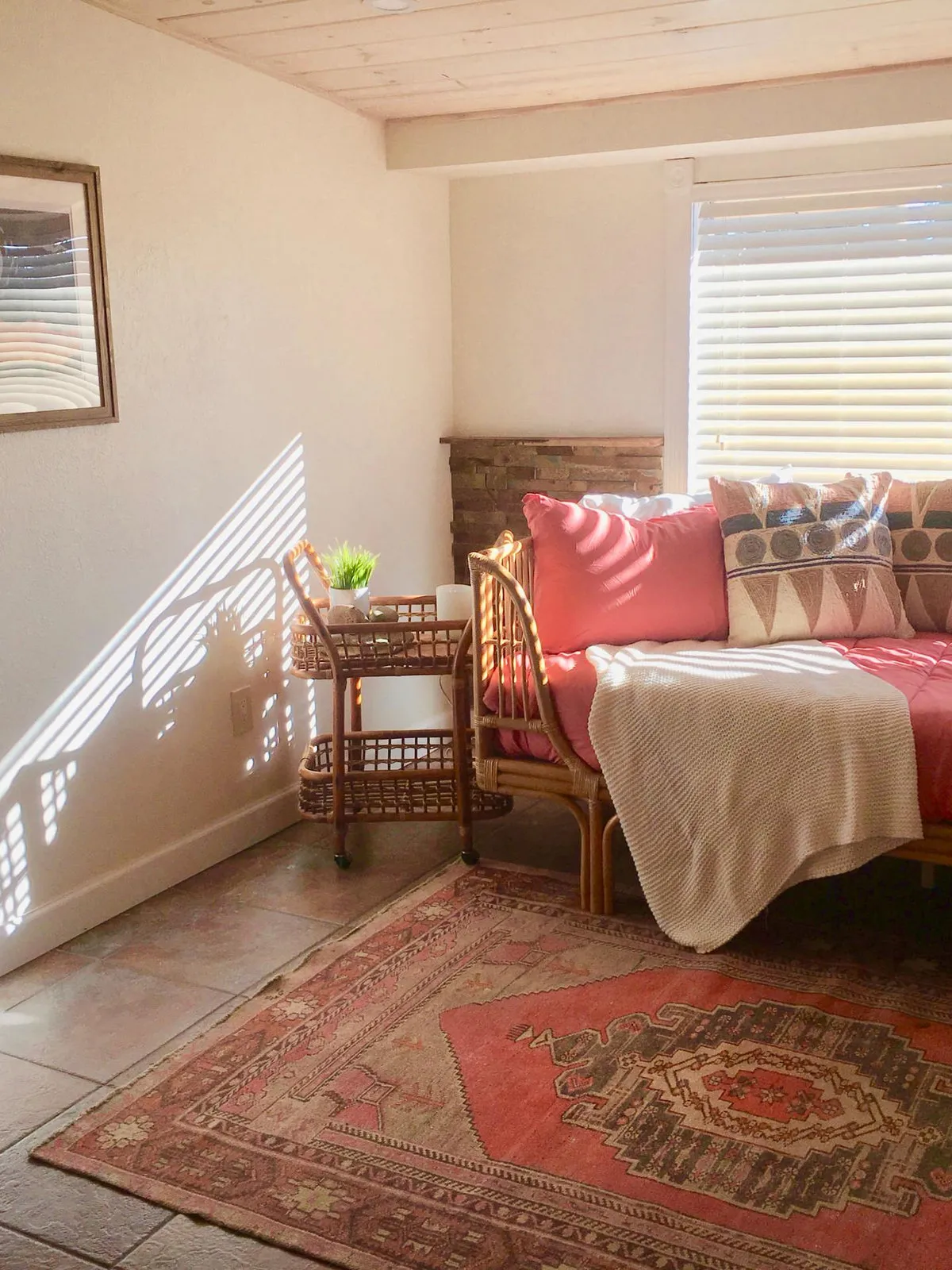 Woven daybed with coral and patterned cushions beside a small woven side table