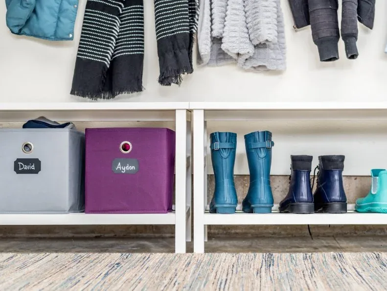 White low cubbies containing labeled colored bins beside a group of upright rain boots.