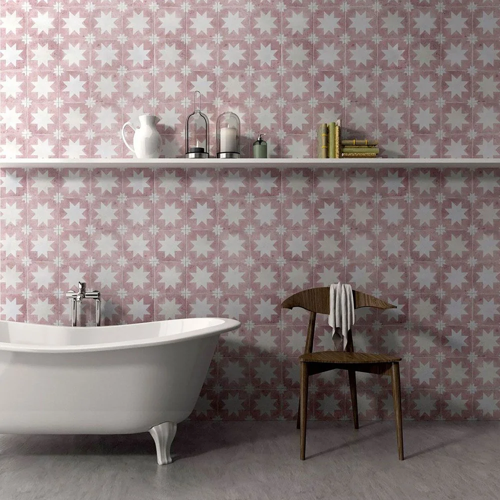 Pink and white star-patterned tiles cover the wall above a white freestanding bath and a wooden chair