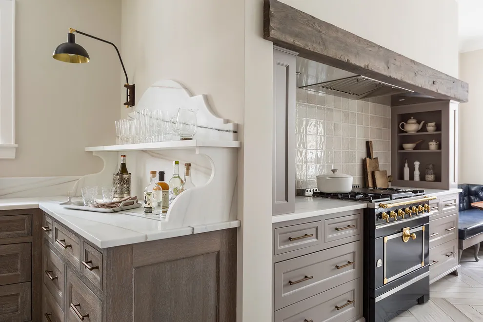 Taupe lower cabinets flank a range beneath a timber beam and a pale hood
