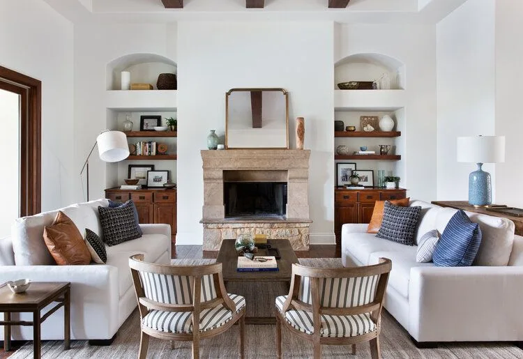 Pale block-style fireplace between arched shelf recesses and wood cabinets, with facing white sofas and striped chairs