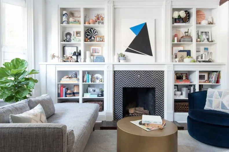 White divided built-ins around dark herringbone fireplace with geometric picture and pale sofa
