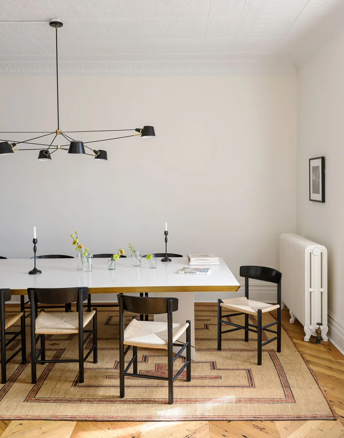 Thin black multi-arm light above a pale rectangular table with dark chairs in a white dining room