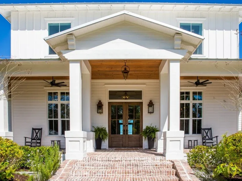 White country house with gabled entrance, wood double doors, paired lanterns and brick approach
