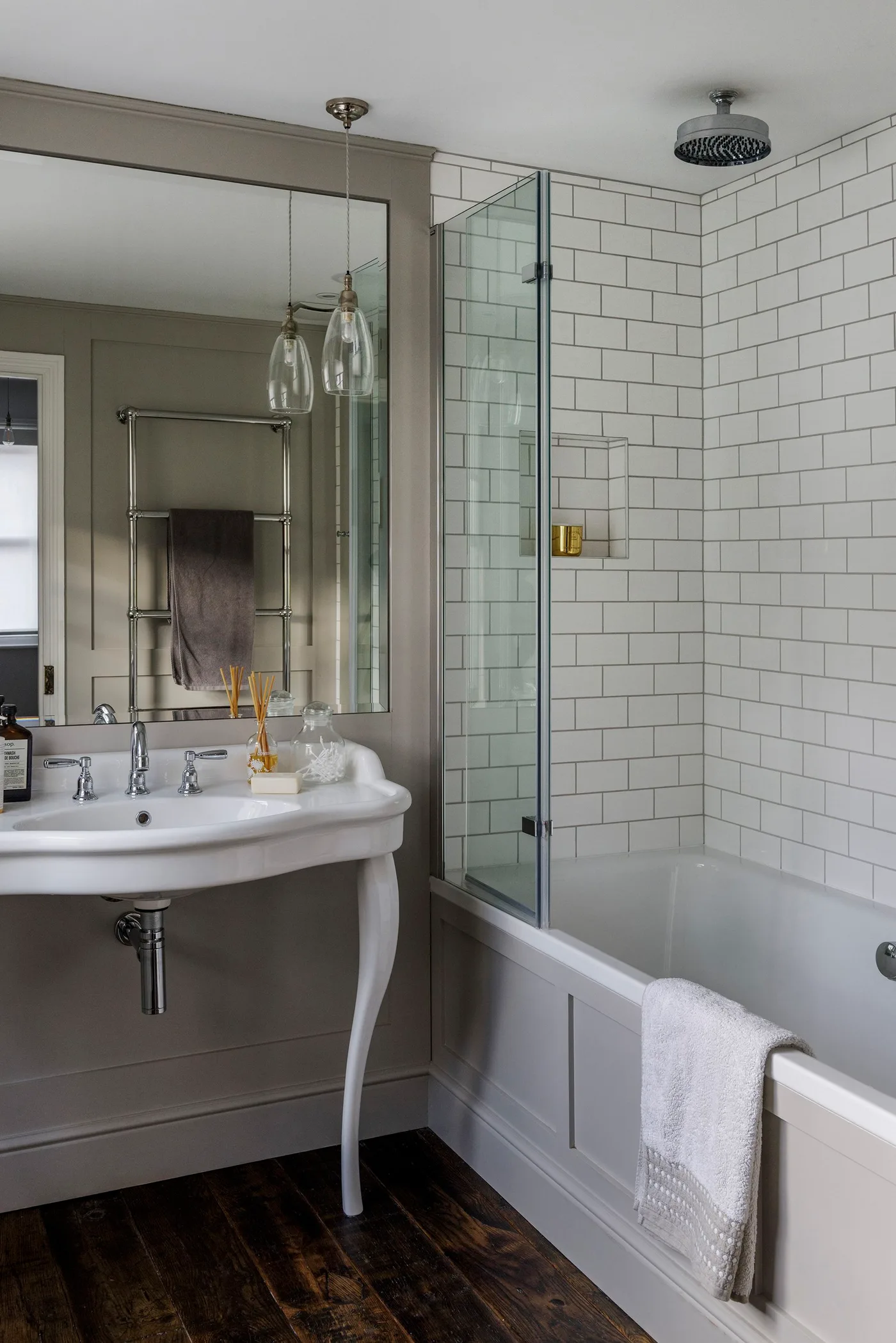 Bathroom with white subway tiles above an inset bath, clear shower screen and a curved wall-hung basin.