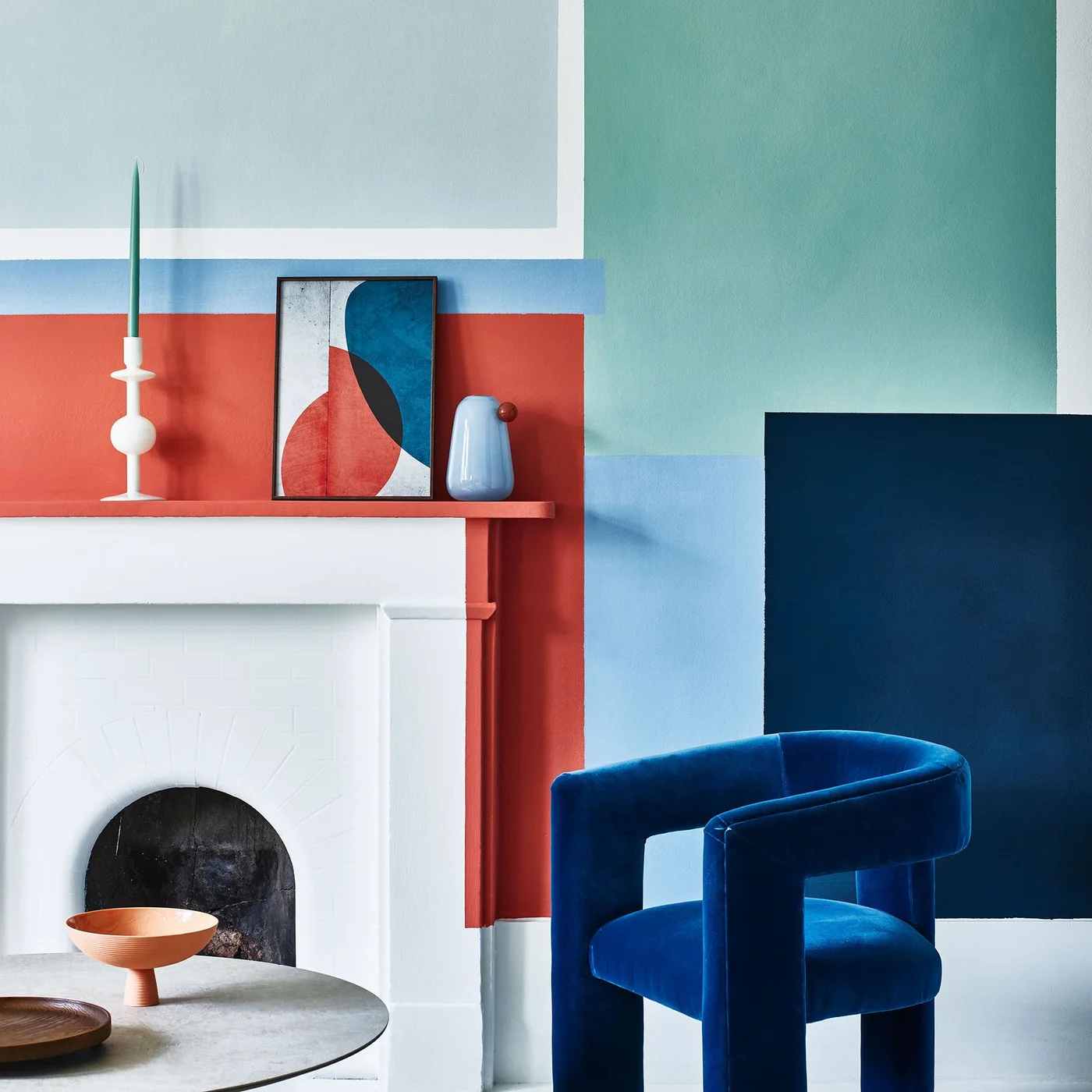 Coral, blue and green painted blocks surround a white fireplace beside a blue armchair and round table