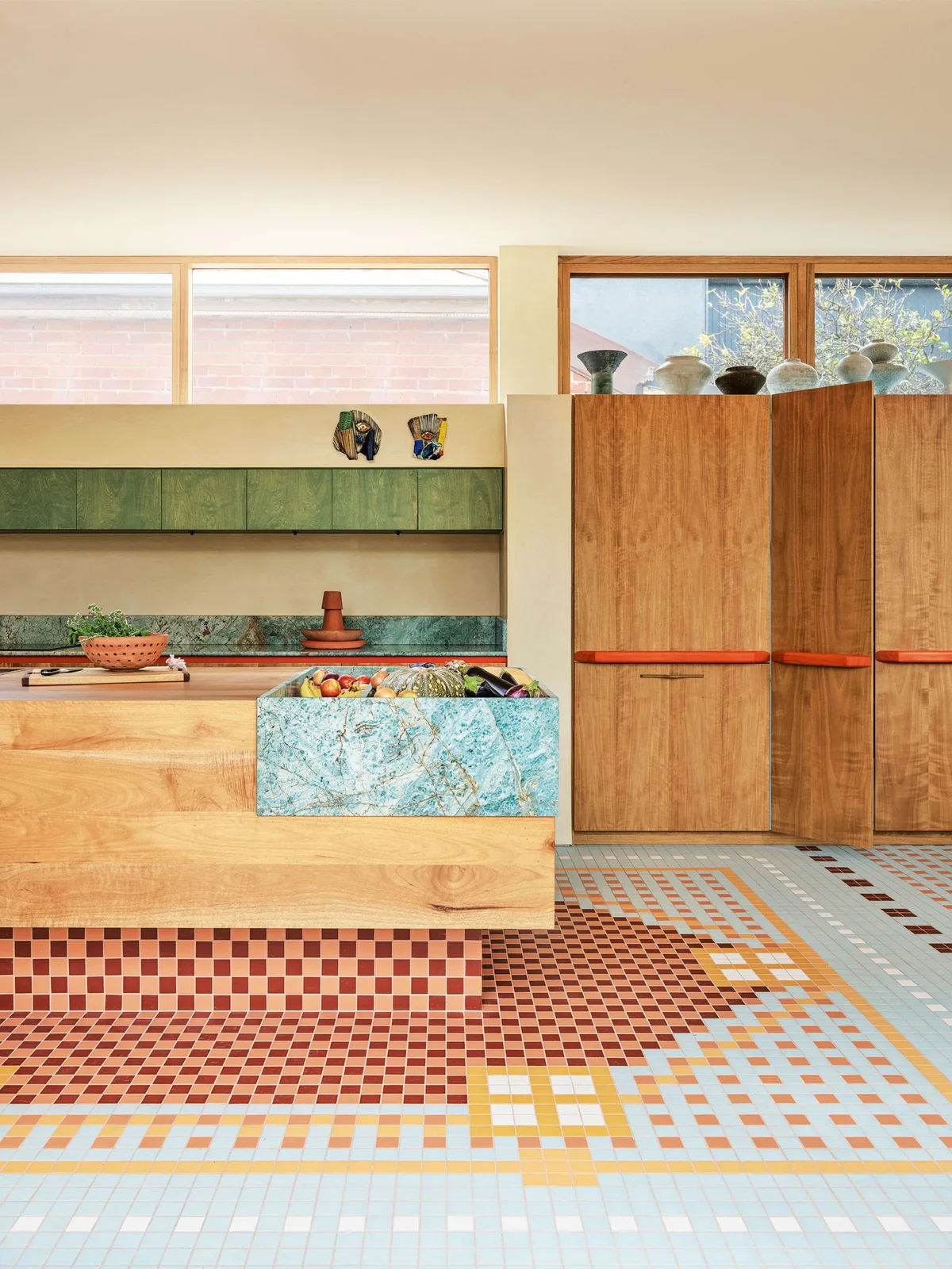 A turquoise veined island detail sits above a multicolored geometric floor beside wood-toned cabinets with red handles and green upper cupboards