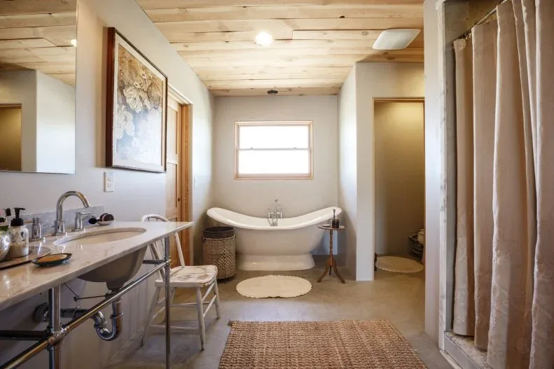 Wood-paneled bathroom ceiling above a pale curved bath, open washstand and beige shower curtain