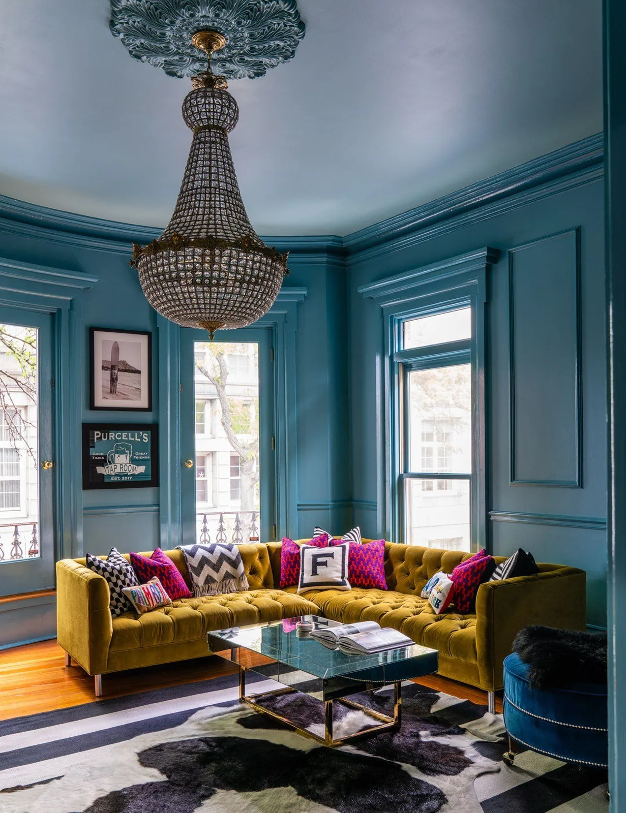 Blue paneling rises behind a yellow sofa with pink accents under a decorative pendant.