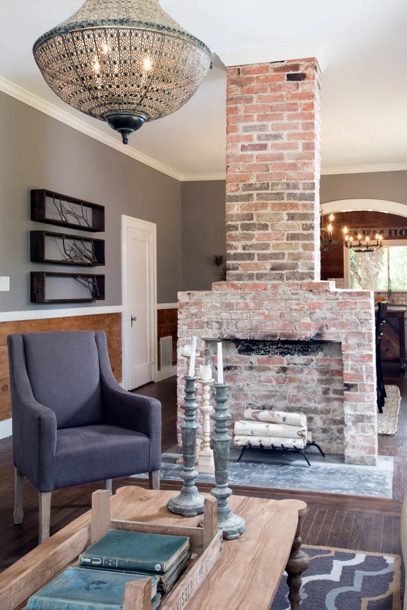 Freestanding stepped brick fireplace between gray sitting area and adjoining room with dark floor