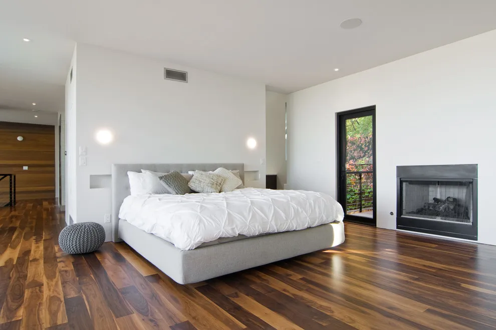 A pale upholstered bed sits on a dark wood floor with visible tonal variation