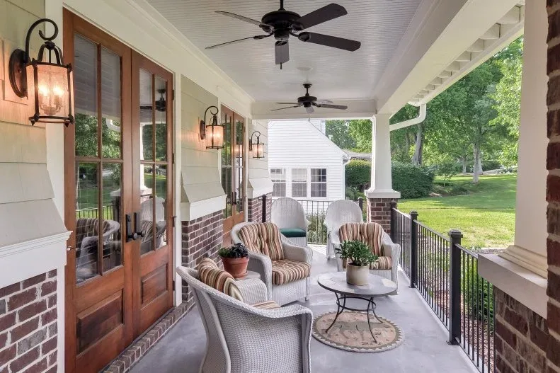 White woven porch chairs with striped cushions beside wood glazed doors, wall lanterns and ceiling fans